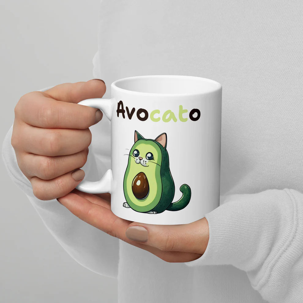 White mug with avocado-themed design held by a person against a gray background