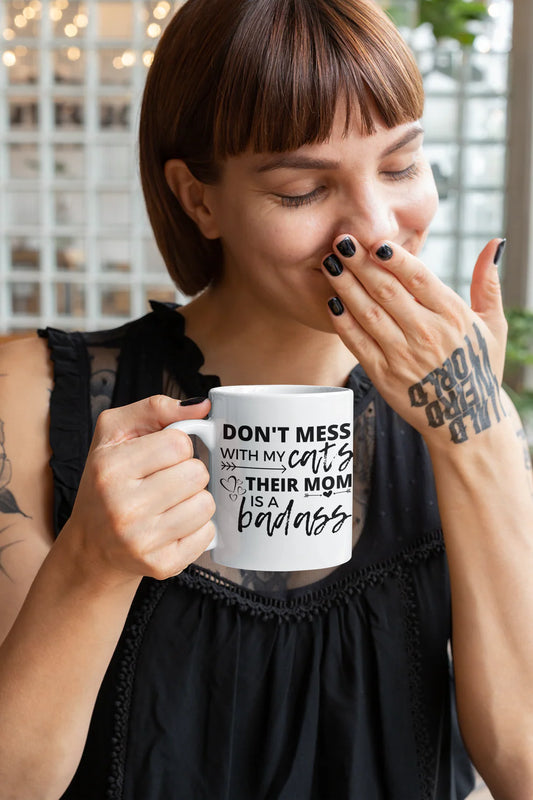 Person holding a mug with text, wearing a black sleeveless top.