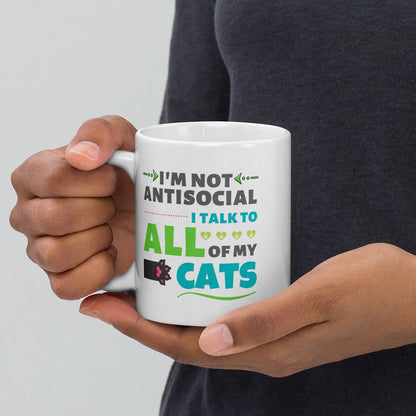 Person holding a white mug with humorous text about cats on a plain background