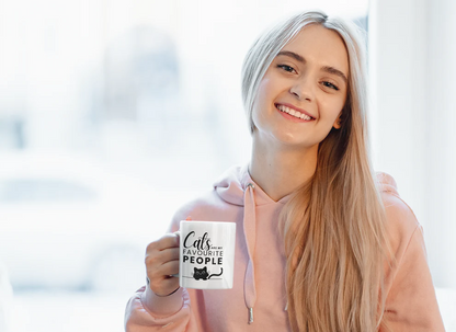 Woman holding a mug with 'Cats are my favorite people' text, smiling in a blurred indoor setting