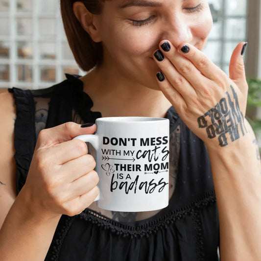 Person holding a mug with text about cats and their mom, in an indoor setting.