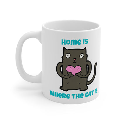 White mug with a black cat holding a pink heart and text 'Home is where the cat is' on a white background