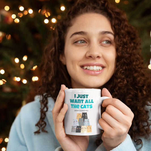Woman holding a mug with a cat-themed design in front of a decorated Christmas tree.